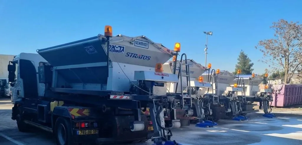 משאיות לפיזור מלח עומדות בשורה בחניון, ערוכות לקראת אירוע השלג
