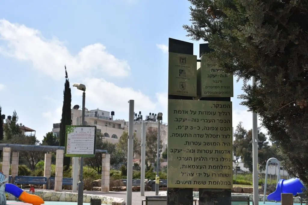 שלט מתכת בכניסה לגן הגבורה, עם סמלי המדינה, קק"ל ועיריית ירושלים, ועליו כיתוב שפונה למבקר ואומר שרגליו עומדות על אדמת הכפר העברי נווה יעקב, ושמצפון, כשלושה קילומטרים משם, היה המושב עטרות. מאחורי השלט גן משחקים עם מגלשות צבעוניות, פרגולה עם ספסלים ובנייני מגורים