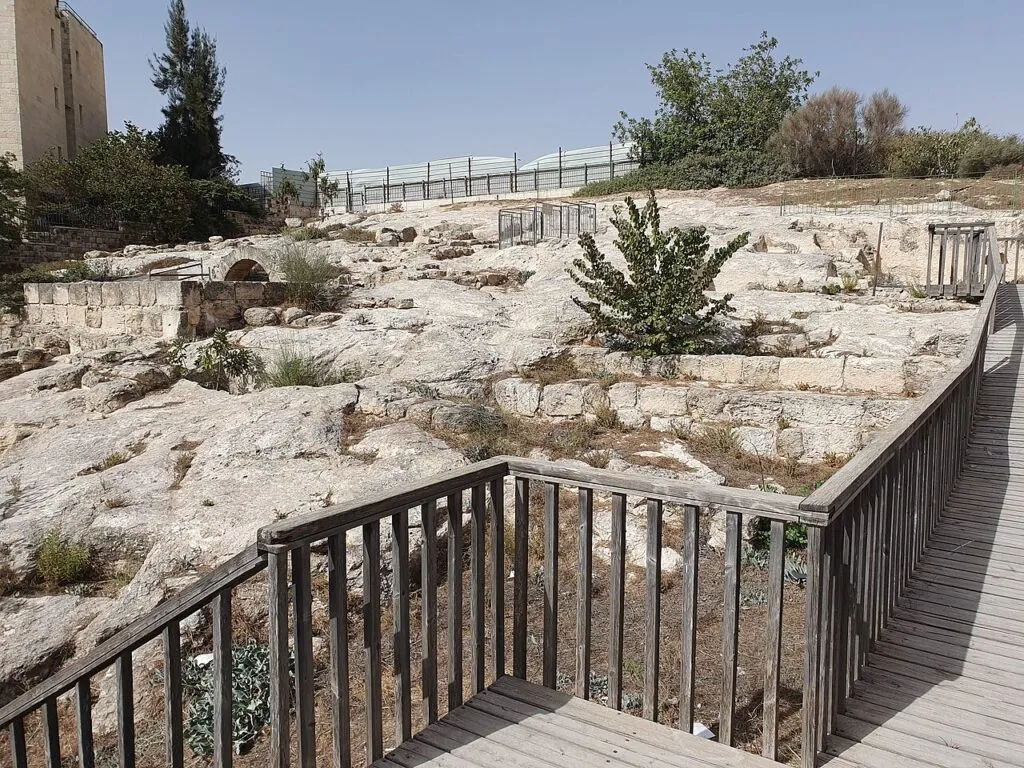 גן הידע בפסגת זאב: שביל עץ עם מעקה עובר מעל משטחי סלע חצובים ושרידי קירות עתיקים