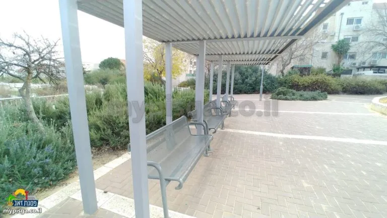 פרגולה עם ספסלי מתכת לאורך שביל מרוצף בגינת טוניק