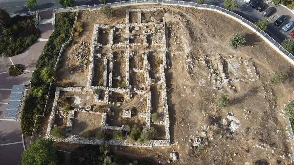 מבט מלמעלה על מנזר הצבאים: מלבן של קירות אבן נמוכים שמחולק לחדרים רבים, לידו עוד שרידי קירות על שטח עפר, ובפינה מכוניות חונות ושבילים