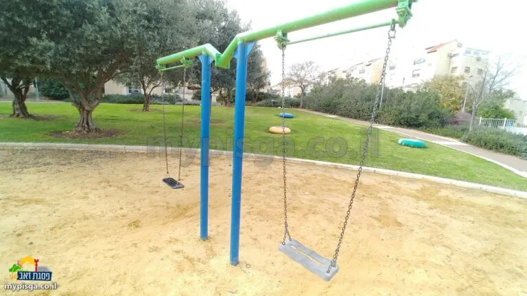 נדנדות בארגז חול בגינת טוניק, ומאחוריהן מדשאה ועצי זית
