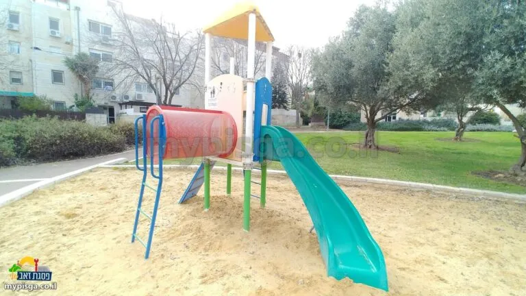 מתקן משחק עם מנהרה אדומה ומגלשה ירוקה בארגז חול, עצי זית ברקע