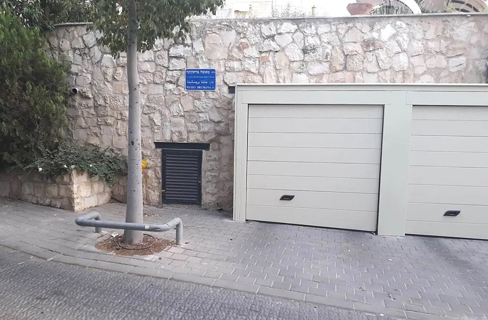 שלט הרחוב מאשה ברוסקינה על קיר אבן, ליד דלתות חניה, בפסגת זאב
