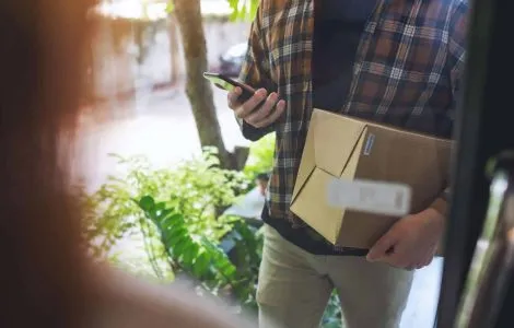 Closeup image of a delivery man with mobile phone holding parcel box to delivery